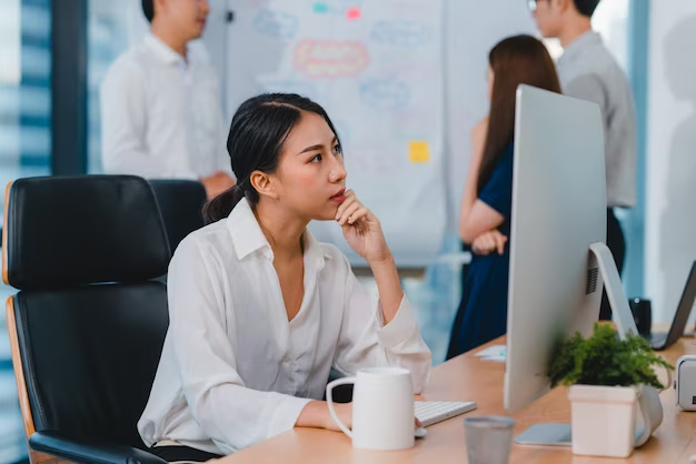 Woman in front of a computer monitor, holding her chin as if deep in thought