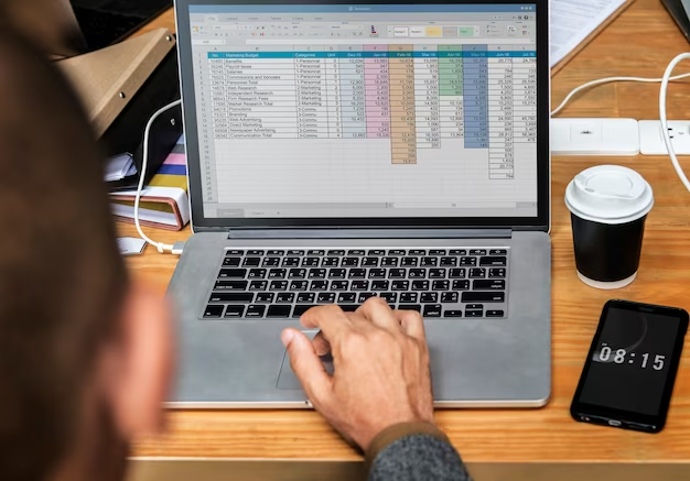 A man works on a laptop on which there is a table with data